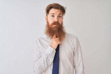 Genç kızıl saçlı İrlandalı işadamı, izole edilmiş beyaz arka planda durup parmakları çenesinde şüpheyi düşünüp kafasını kaldırıyor.