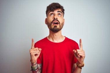 İzole edilmiş beyaz arka plan üzerinde duran kırmızı tişörtlü genç adam şaşırmış ve şaşırmıştı. Parmaklarıyla işaret ediyor ve kollarını kaldırıyordu..