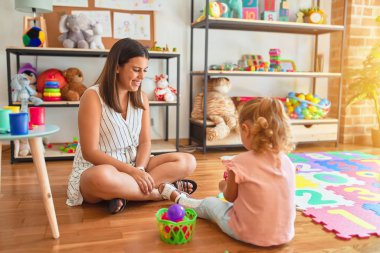 Güzel öğretmen ve sarışın yeni yürümeye başlayan kız anaokulunda plastik meyve, sebze ve yemekle oynuyor.