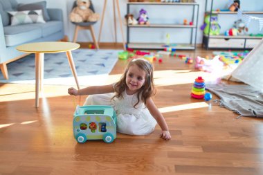 Sevimli sarışın çocuk gülümsüyor. Anaokulunda oyuncaklarla oynarken mutlu oluyor.