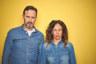 Güzel orta yaşlı çift, izole edilmiş sarı arka plan üzerinde birlikte duruyorlar şüpheci ve gergin, sorun yüzünden suratları asık. Negatif kişi.