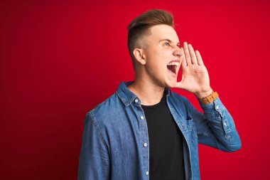 İzole edilmiş kırmızı arka plan üzerinde duran kot gömlekli genç yakışıklı adam el ele tutuşarak bağırıyor ve bağırıyordu. İletişim konsepti.