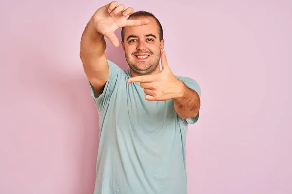 青いカジュアルなTシャツを着た若者がピンクの背景に立って 手と指で幸せな顔でフレームを作って笑っています 創造性と写真の概念 — ストック写真