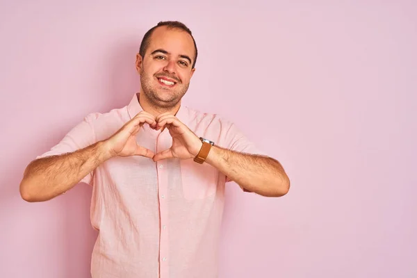 年轻男子穿着典雅的衬衫 站在孤立的粉色背景上 微笑着 用双手做着心形符号 浪漫的概念 — 图库照片