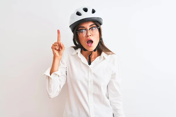 Beautiful businesswoman wearing glasses and bike helmet over isolated white background pointing finger up with successful idea. Exited and happy. Number one.