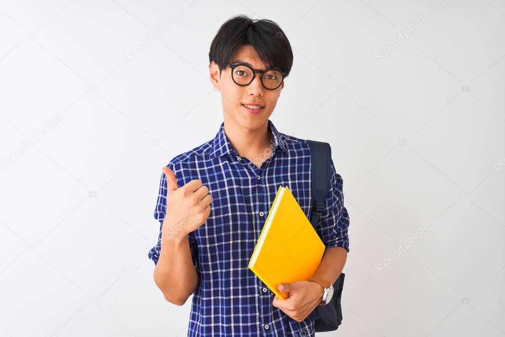 Chinese student man wearing backpack holding notebook over isolated white background happy with big smile doing ok sign, thumb up with fingers, excellent sign