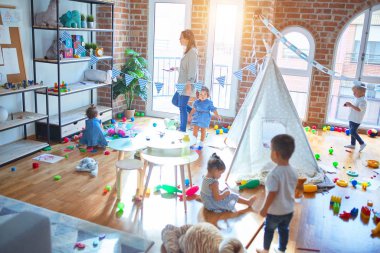 Güzel öğretmen ve bir grup çocuk anaokulunda bir sürü oyuncakla oynuyorlar.