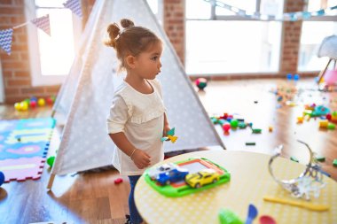 Anaokulunun masasında çatal bıçak ve yemek oyuncaklarıyla oynayan genç ve güzel bir çocuk.