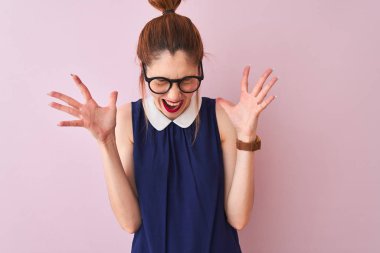 Atkuyruklu, zarif bir elbise ve gözlük takan kızıl saçlı bir kadın izole edilmiş pembe arka planda başarı için çılgın ve çılgın kutlamalar yapıyor. Kolları havada ve gözleri kapalı bağırıyor. Heyecanlı. Kazanan konsept