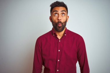 İzole edilmiş gri arka planda duran kırmızı şık gömlekli genç Hintli adam dudaklı balık suratı yapıyor, çılgınca ve komik bir jest. Komik ifade.