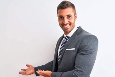 Takım elbiseli ve kravatlı genç yakışıklı iş adamı izole edilmiş arka planda gülümseyerek içeri girmeye davet ediyor.