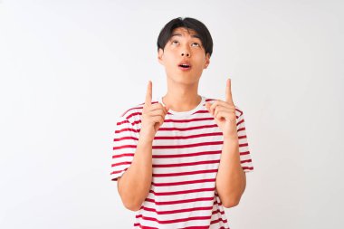 Izole beyaz arka plan üzerinde duran rahat çizgili t-shirt giyen genç Çinli adam şaşırttı ve yukarı bakarak ve parmakları ile işaret ve kolları kaldırdı şaşırttı.