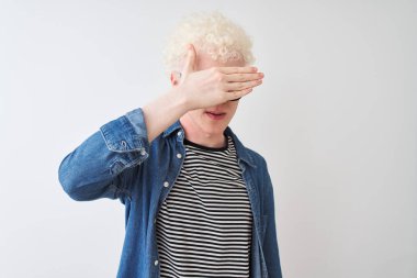 Kot gömlek ve gözlük takan genç albino sarışın adam izole edilmiş beyaz arka planda gözlerini eliyle kapatıyor, ciddi ve üzgün görünüyor. Görme, saklama ve reddetme konsepti