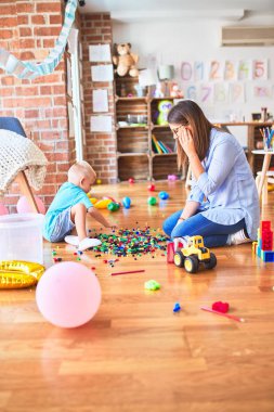 Genç beyaz çocuk öğretmeniyle oyun okulunda oynuyor. Anne ve oğlu oyun odasında oyuncak blokları olan bir kuleyi şişiriyorlar.