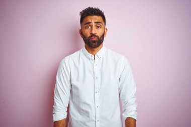 Genç Hintli iş adamı zarif bir gömlek giyer ve pembe arka planda dikilip komik yüzlü yanakları şişirir. Havayla şişmiş ağız, çılgın bir ifade..