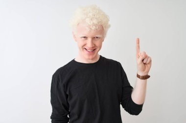 Siyah tişörtlü genç albino adam izole edilmiş beyaz arka planda duruyor ve bir numarayı işaret ediyor kendinden emin ve mutlu bir şekilde gülümsüyor..