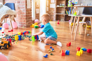 Anaokulunda oyuncak bloklarıyla oynayan beyaz bir çocuk. Anaokulu çocuğu oyun odasında kule inşa etmekten mutlu.