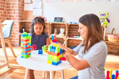 Güzel öğretmen ve küçük kız anaokulunda inşaat bloklarıyla oynuyorlar.