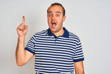 Sıradan çizgili polo giyen genç adam izole edilmiş beyaz arka planda durup başarılı bir fikri işaret ediyor. Heyecanlı ve mutlu. Bir numara..