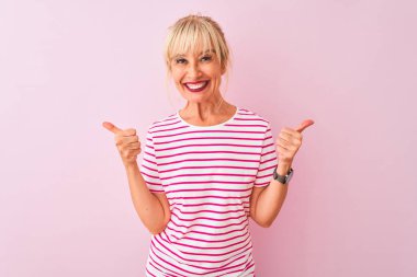 İzole edilmiş pembe arka plan başarısı tabelasının üzerinde duran çizgili tişört giyen orta yaşlı bir kadın elleriyle olumlu jest yapıyor, gülümsüyor ve mutlu. Neşeli ifade ve kazanan jest.