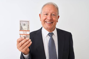 Gri saçlı kıdemli işadamı, izole edilmiş beyaz arka planda dolar tutan takım elbiseli mutlu bir yüzü olan ve kendine güvenen bir gülümsemeyle dişlerini gösteren bir gülümseme takınıyor.