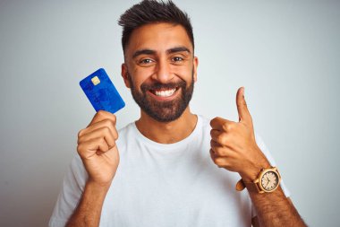 Genç Hintli müşteri kredi kartı tutuyor. İzole edilmiş beyaz arka planda duruyor. Kocaman gülümsüyor.