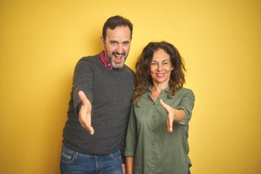 Izole sarı arka plan üzerinde Güzel orta yaş çift tebrik ve karşılama olarak dostça sunan el sıkışma gülümseyerek. Başarılı iş.