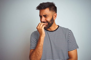 Siyah çizgili tişört giyen genç Hintli adam izole edilmiş beyaz arka planda duruyor. Ağzı tırnak yiyen elleri gergin ve stresli görünüyor. Endişe sorunu.