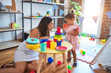 Genç, güzel öğretmen ve bebek, anaokulundaki masada halkalar kullanarak piramit inşa ediyorlar.