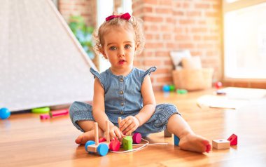 Renkli oyun odasında beyaz güzel bir bebek oyuncaklarla oynuyor. Anaokulundaki ahşap tren parçalarıyla mutlu ve eğlenceli..