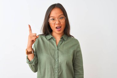 Young chinese woman wearing green shirt and glasses over isolated white background pointing finger up with successful idea. Exited and happy. Number one.
