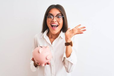 Gözlüklü güzel bir iş kadını, kumbarasını izole edilmiş beyaz arka planda tutuyor. Çok mutlu ve heyecanlı. Kazanan ifade zaferi büyük bir gülümsemeyle kutluyor ve ellerini kaldırıyor.