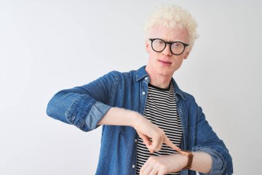 İzole edilmiş beyaz arkaplan üzerine kot gömlek ve gözlük takan genç albino sarışın adam. Aceleyle saati, sabırsızlığı, son teslim tarihini geciktirdiği için üzgün ve kızgın olduğunu gösteriyor.