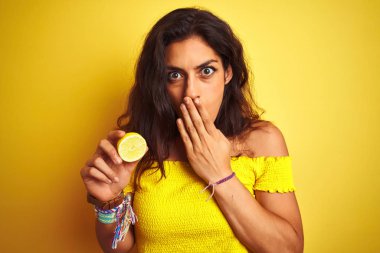 Ortadaki limonu tutan genç ve güzel bir kadın izole edilmiş sarı arka planda duruyor. Ağzı kapalı, utancından ağzı açık, korkusunun dışa vurumu, sessizlikten korkması, gizli konsept.