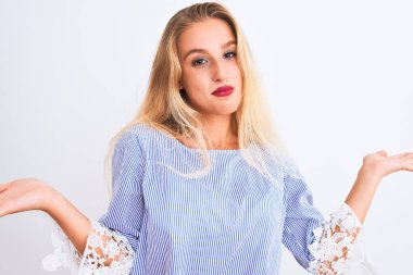 Zarif mavi tişört giyen genç ve güzel bir kadın soyutlanmış beyaz arka plan üzerinde duruyor. Kolları ve elleri havada, kafası karışmış bir ifade. Şüphe kavramı.