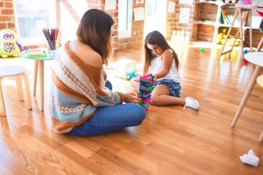 Anaokulunda bir sürü oyuncağın etrafında tahta bloklarla oynayan güzel öğretmen ve bebek.
