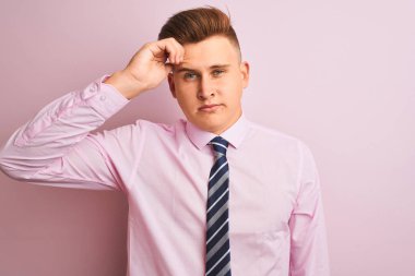 Gömlek ve kravat takan genç yakışıklı iş adamı pembe arka planda duruyor. Alnındaki sorun yüzünden endişeli ve stresli. Kriz konusunda endişeli.