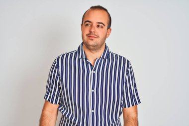 Mavi çizgili tişört giyen genç adam izole edilmiş beyaz arka planda duruyor gülümsüyor ve başka tarafa bakıyor..