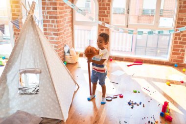Güzel Afrikalı Amerikalı çocuk anaokulunda bir sürü oyuncakla at oyuncağıyla oynuyor.
