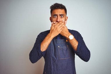Önlük giyen genç Hintli işçi, izole edilmiş beyaz arka planda dikiliyor. Ağzını yanlışlıkla ellerle kapatıyor. Gizli konsept.