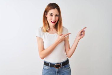 İzole beyaz arka plan üzerinde ayakta rahat t-shirt giyen güzel Redhead kadın gülümseyen ve yan iki el ve parmak ile işaret kamera bakıyor.