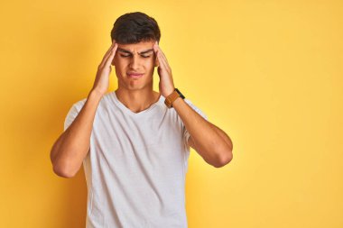 İzole edilmiş sarı arka plan üzerinde duran beyaz tişörtlü genç Hintli adam. Baş ağrısı çekiyor çünkü. Migren ağrısı..