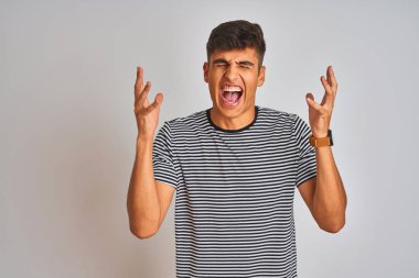 İzole edilmiş beyaz arka planda duran donanma çizgili tişört giyen genç Hintli adam başarı için deli ve çılgın bir kutlama yapıyor kolları havada ve gözleri kapalı heyecanla bağırıyor. Kazanan konsept