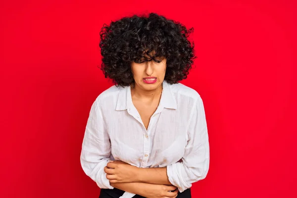 年轻的阿拉伯女人 卷曲的头发 身穿白色休闲衫 背负孤立的红色背景 手放在肚子上 因为恶心 痛苦的疾病感觉不适 阿切概念 — 图库照片