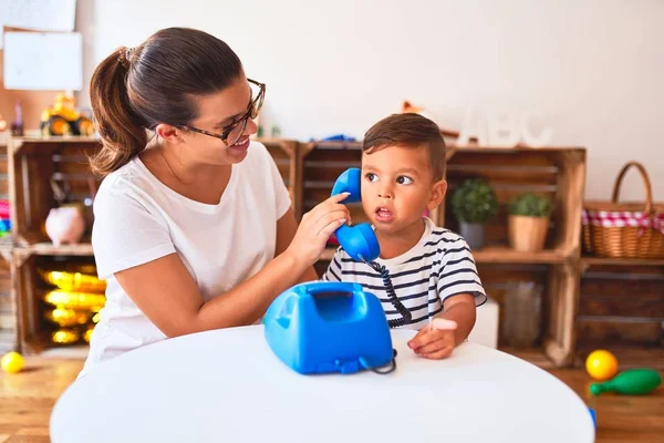 Güzel öğretmen ve küçük çocuk anaokulunda klasik mavi telefonla oynuyor.