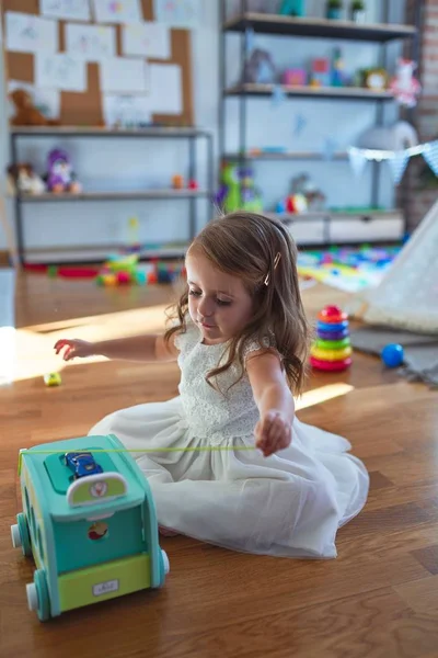 Anaokulunda bir sürü oyuncağın etrafında arabayla oynayan sevimli sarışın çocuk.