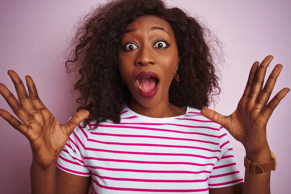Genç Afro-Amerikalı kadın, çizgili tişört giymiş, pembe arka planda durmuş çılgın ve hayret verici başarısını kutluyor, kollarını kaldırmış ve gözleri açık bir şekilde heyecanla haykırıyor. Kazanan konsept
