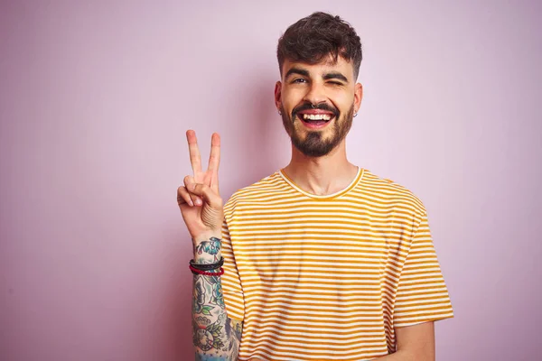 Mladý Muž Tetováním Žlutém Pruhovaném Tričku Stojící Nad Izolovaným Růžovým — Stock fotografie