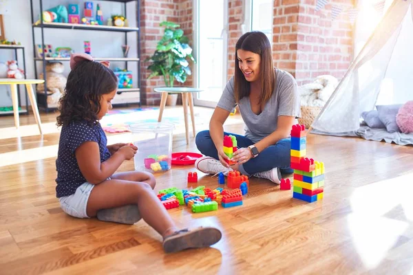 Güzel öğretmen ve küçük kız anaokulunda inşaat bloklarıyla oynuyorlar.