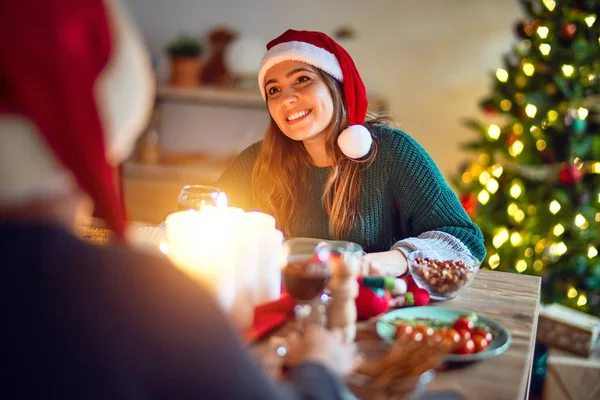 若い美しいカップルの幸せと自信を笑顔 サンタの帽子をかぶった食べ物を食べる家でクリスマスを祝う — ストック写真